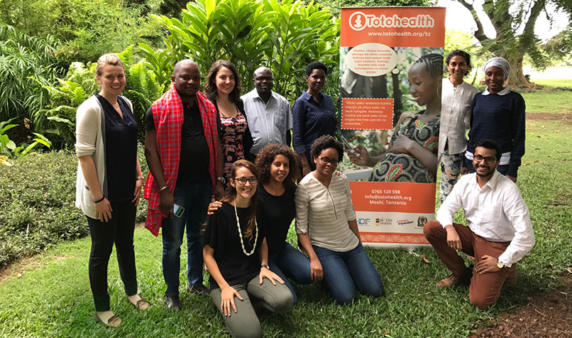 volunteer in Tanzania posing with charity partners in front of information banner